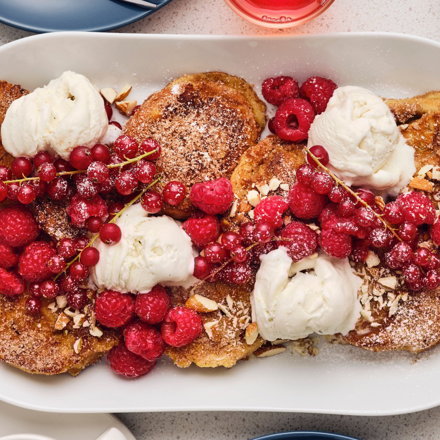 Several pieces of French toast with ice-cream, fresh raspberries, red currants and almonds, are served in a white oval dish.