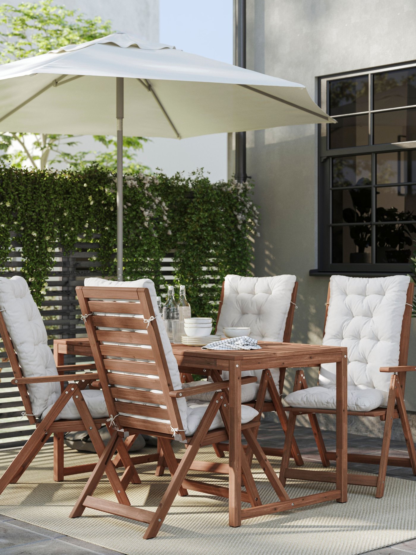 En NÄMMARÖ utomhusmatgrupp i trä med parasoll och vadderade stolar på en terrass.