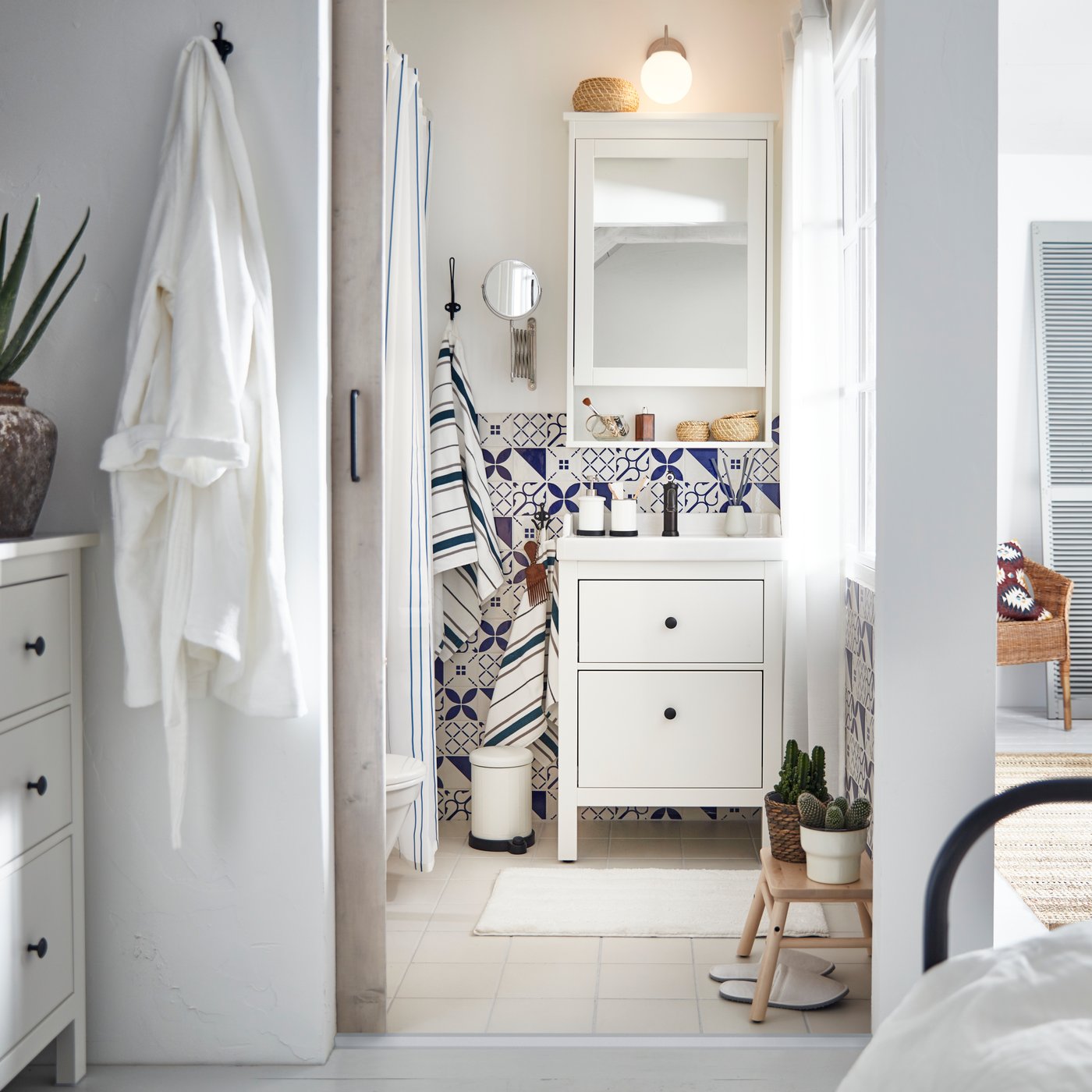 Mała, jasna i przestronna łazienka z płytkami w niebieskie wzory, szafką pod umywalkę IKEA HEMNES/RÄTTVIKEN i szafką ścienną z lustrem.