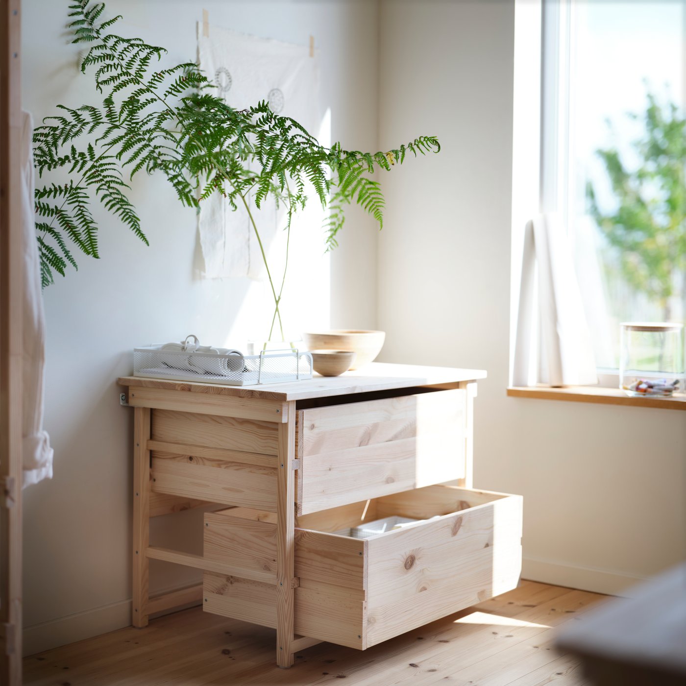 KRONÖREN chest of 2 drawers in pine with plant and bowl on top placed beside a window in a bright bedroom.