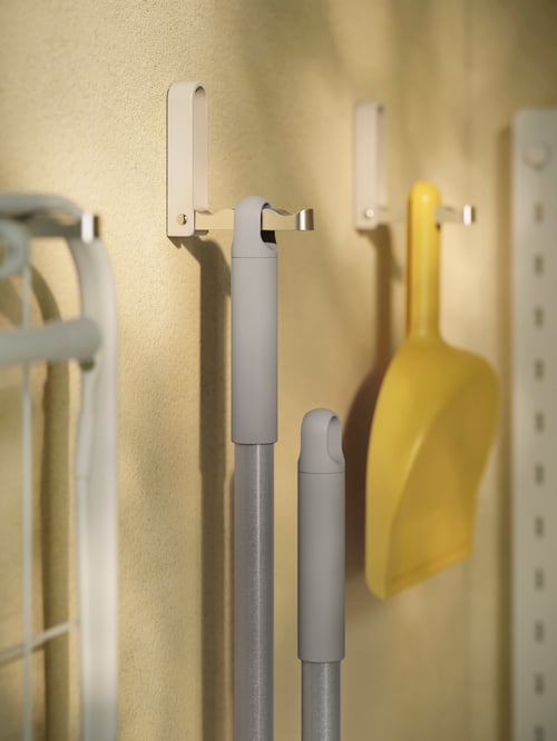 Küche mit drei grauen KLYKET klappbaren Haken an einer Wand. An ihnen hängen u. a. eine PEPPRIG Kehrschaufel und Besen.