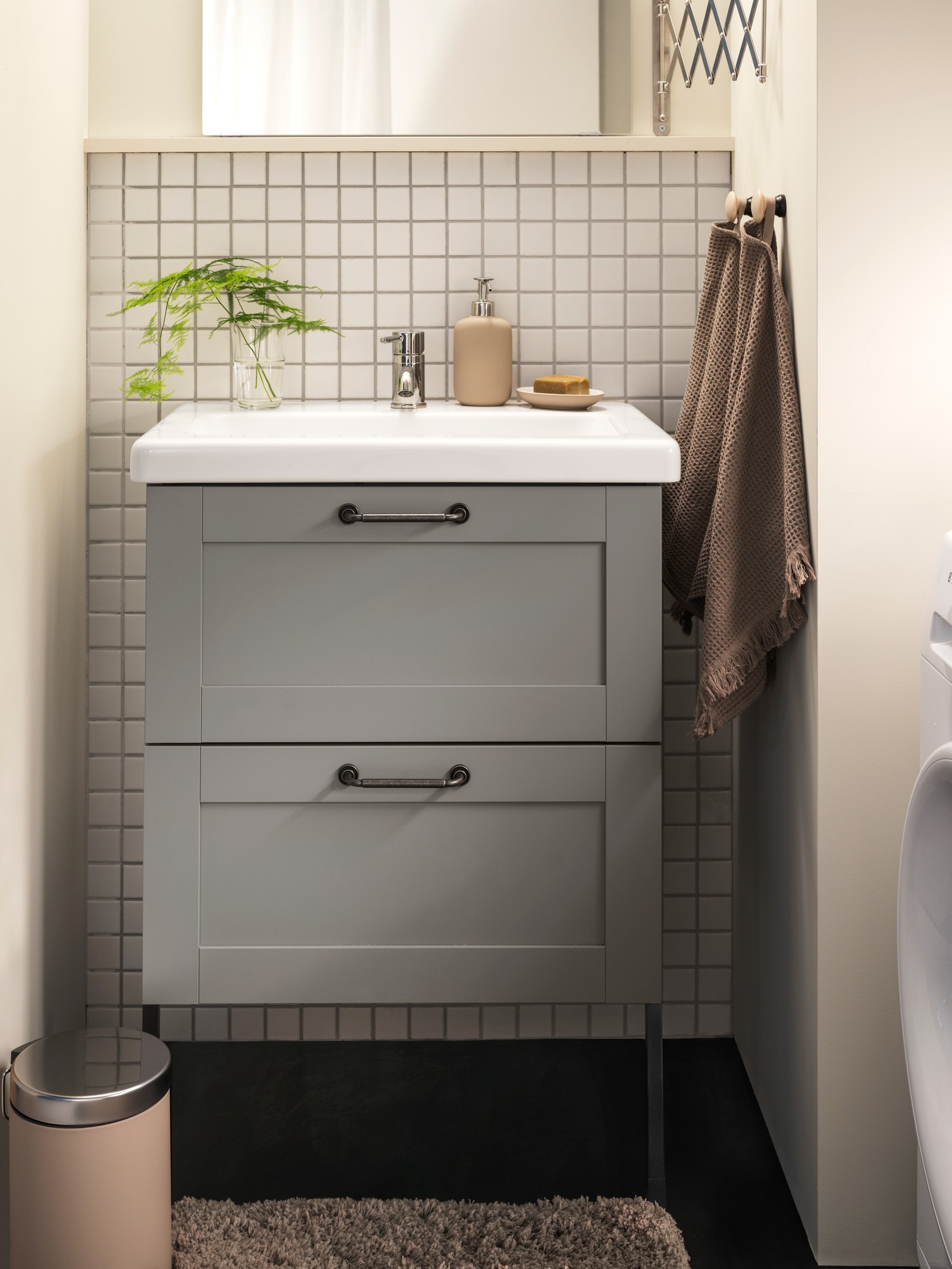Vanitorio de la serie ENHET en color gris, con una toalla de la serie LILLASJON colgada a su lado y una alfombra para baño de la serie ALMTJARN.
