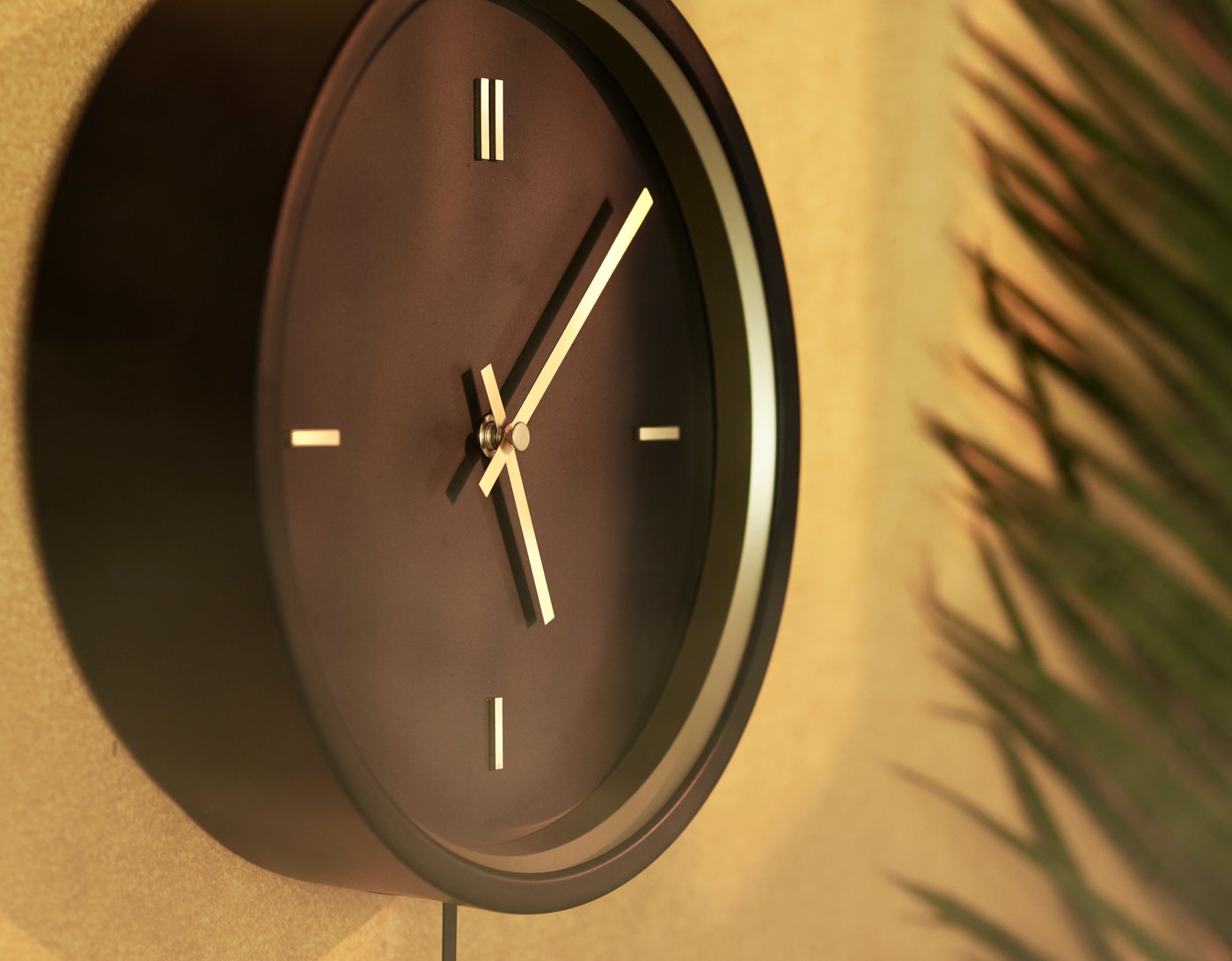 Un primer pla del rellotge de paret STURSK de color negre amb busques i detalls daurats, penjat a una paret de color marró daurat.