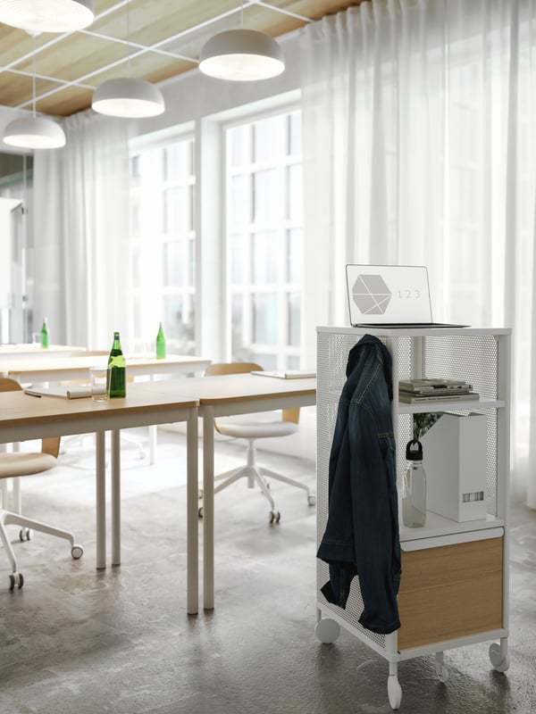 A white storage unit on castors used as a presentation stand in a conference room. A jacket hangs on a hook on its side.