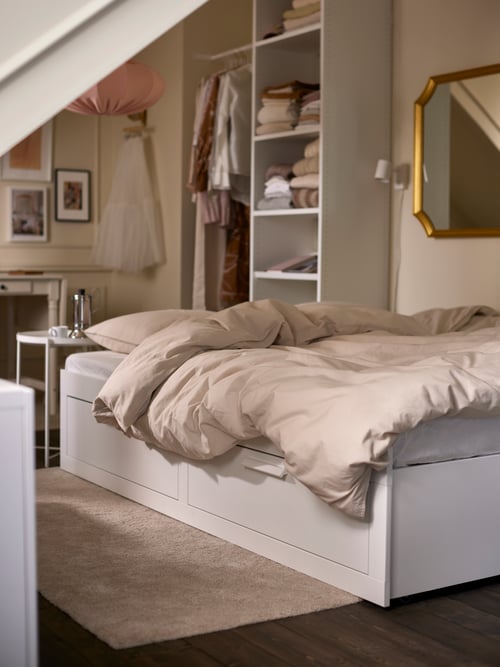 A bedroom featuring a modern Scandinavian day bed frame with two drawers, a beige quilt cover, and a tray table.