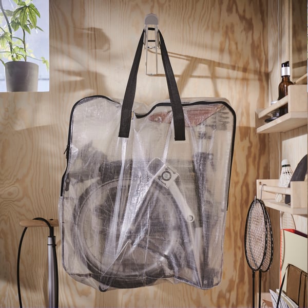 Ein transparenter DIMPA Beutel mit einem Klapprad darin hängt an einer Holzwand.