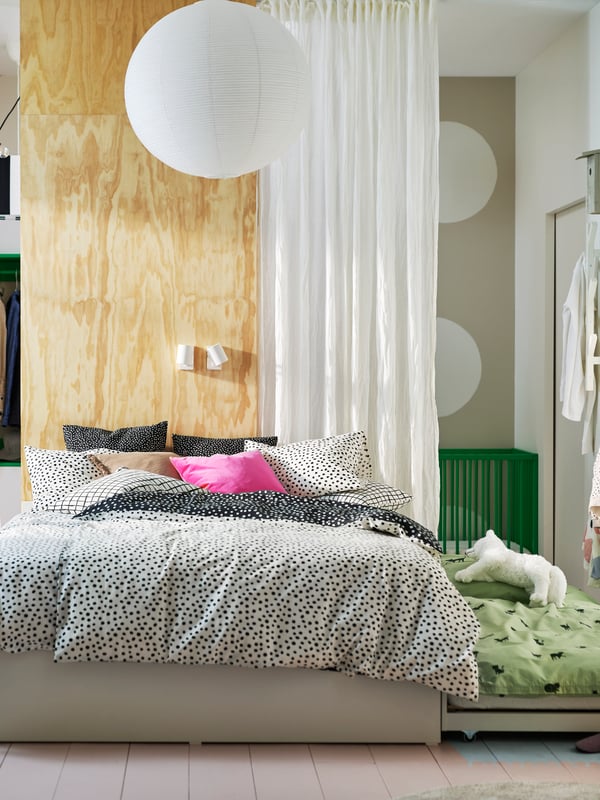 A VIHALS bed with 2 storage boxes and 1 trundle bed covered with black and white BJÖRKGRÅMAL bed linen in a light bedroom.