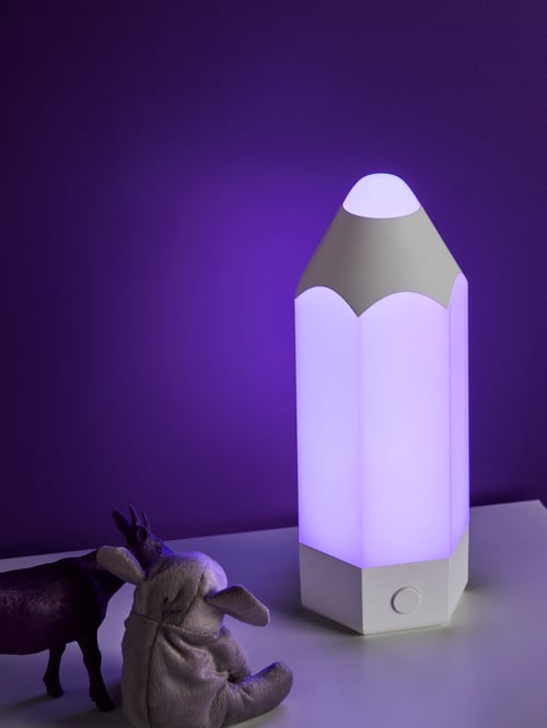 Un plan détaillé d’un bureau dans une chambre d’enfant avec une lampe à DEL en forme de crayon avec une lumière violette à côté de jouets en plastique. 