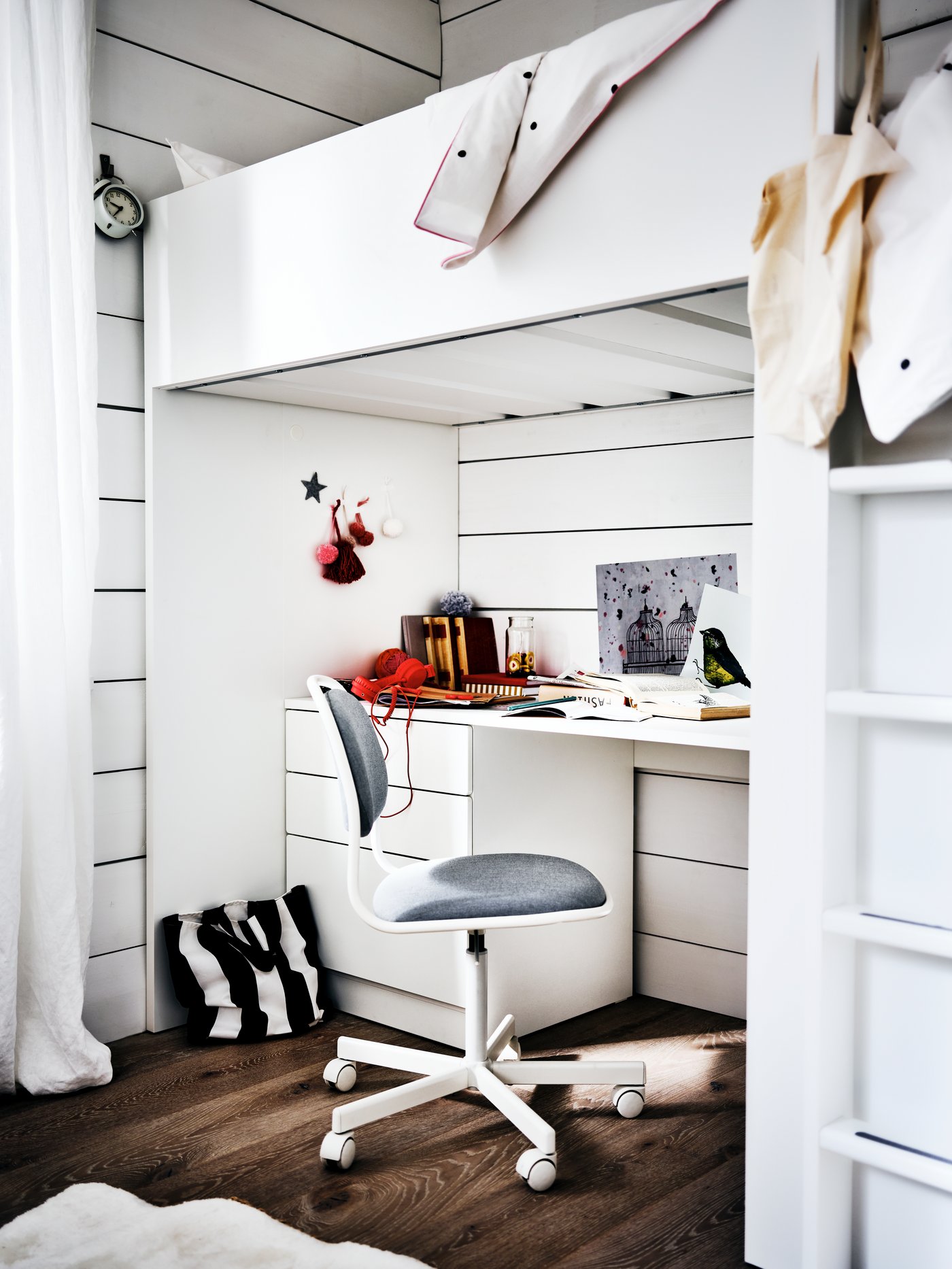 An ÖRFJÄLL chair in front of a white desk that's under a SMÅSTAD loft bed in a white bedroom with a dark wood floor.