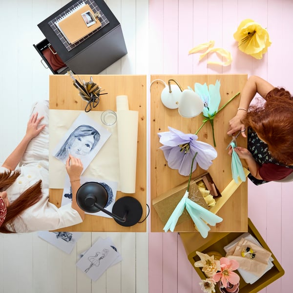 Two BOLLPOJKE desks in pine/white side by side, viewed from above, with two teens crafting and using art supplies.