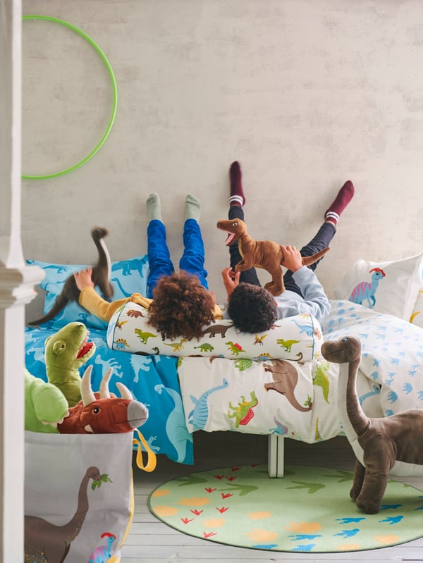 2 Kinder liegen in einem Bett mit Dions und Dino Bettwäsche. 