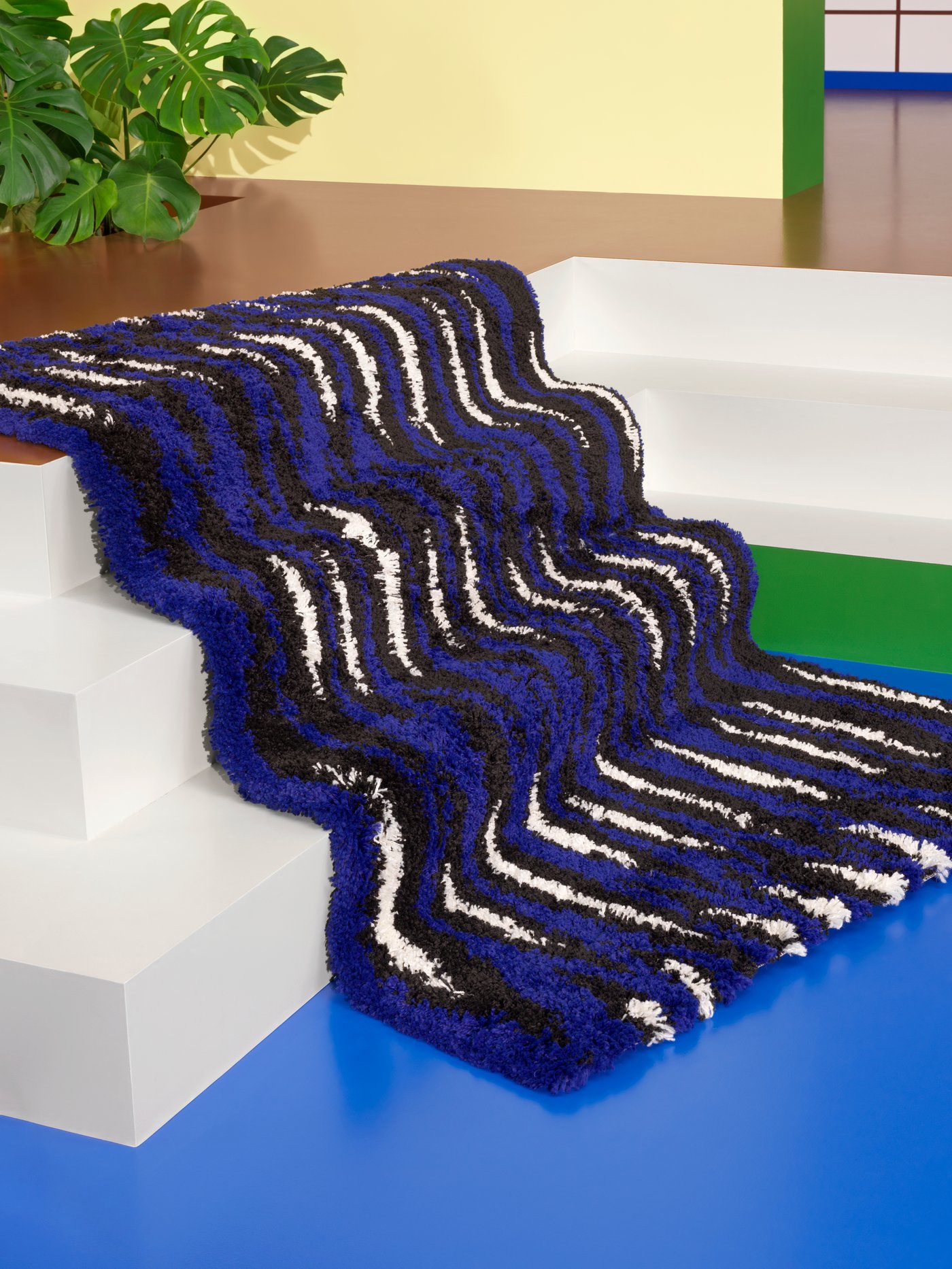 A BULLERREMSA high pile rug in blue-black/white lies draped over a white sunken staircase in a colourful room.