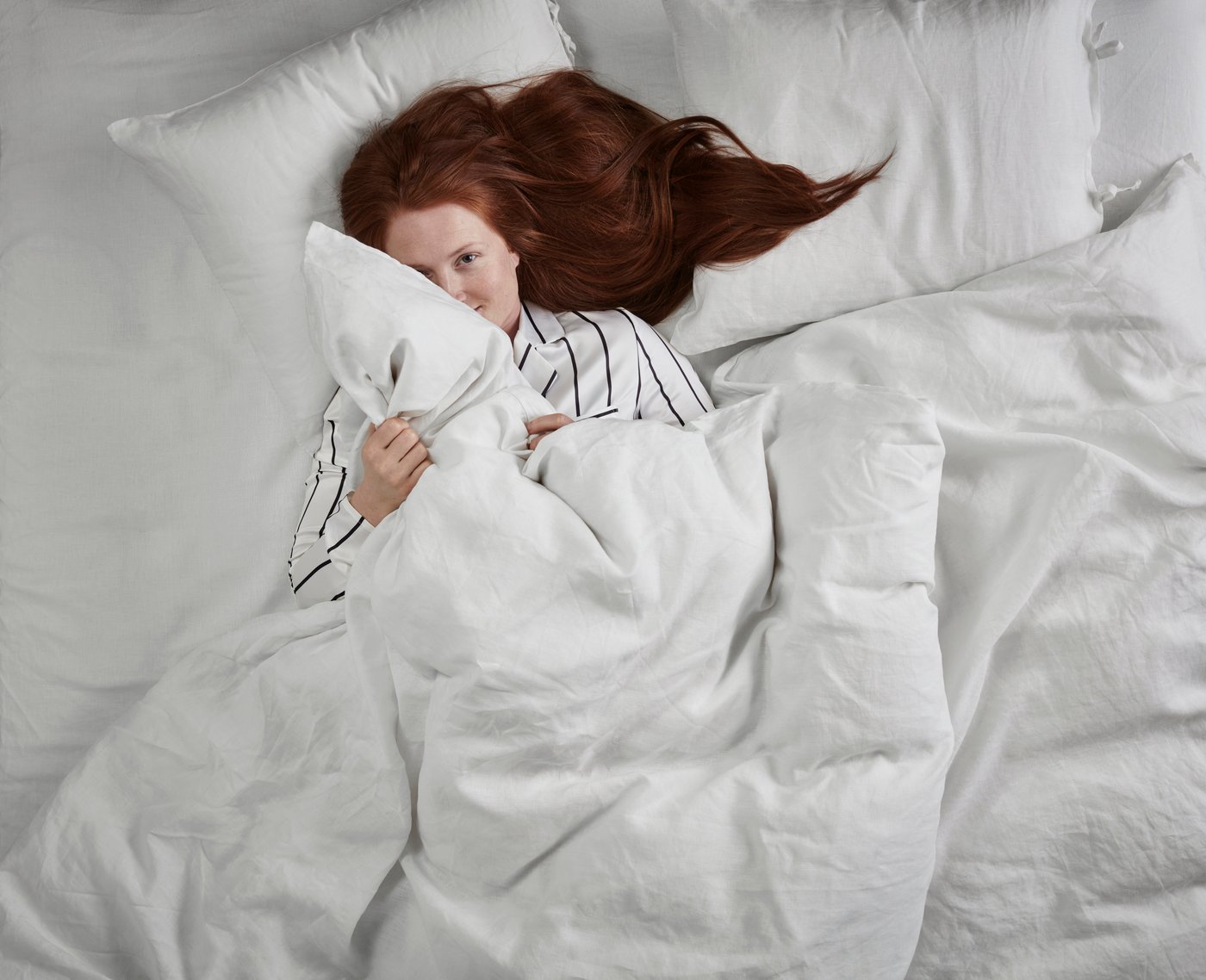 Kobieta leżąca w łóżku z białą pościelą.