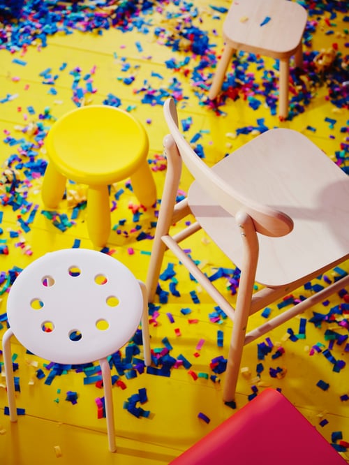 An aerial view of a confetti-covered floor with different stools and a solid birch RÖNNINGE chair that has a curved backrest.