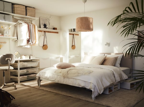 Es ist ein sonniges Schlafzimmer in neutralen Farbtönen mit einem KLEPPSTAD Bettgestell mit heller Bettwäsche und einem LERGRYN Leuchtenschirm über dem Bett zu sehen.