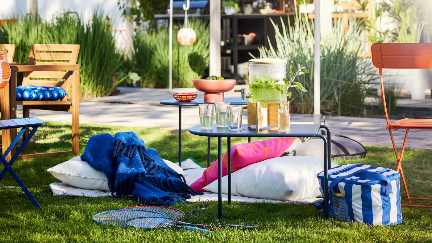 En have med grønne områder og en parasol har et sortblåt GRYTSHOLM indskudsbord, perfekt til udendørs brug.