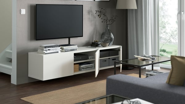 Man sieht ein Wohnzimmer in dem eine weiße TV Bank mit geöffneten Schranktüren an der Wand hängt. Darüber hängt ein TV.