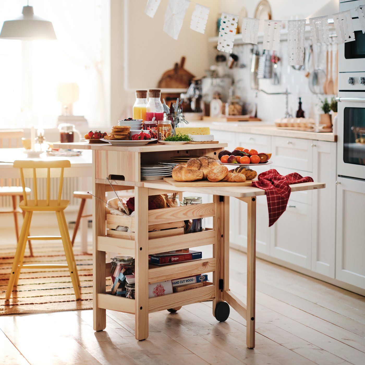 RESARÖ mobile drop-leaf table stocked with breakfast food and tableware placed beside a dining table in a light kitchen.