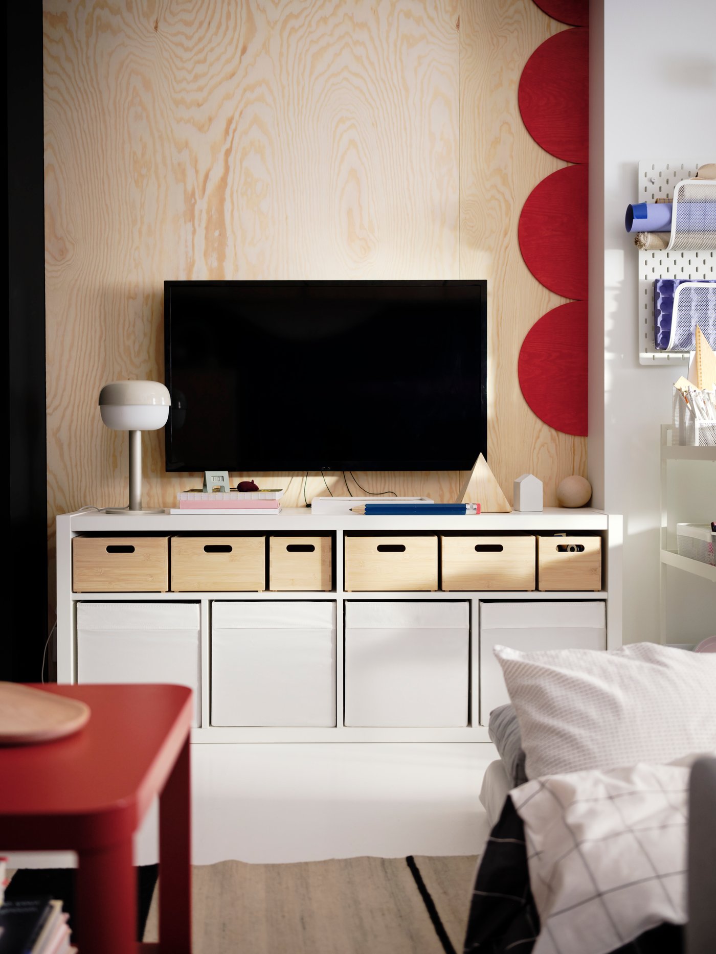 Téléviseur mural au-dessus d’un banc TV KALLAX blanc avec des boîtes de rangement UPPDATERA en bambou clair sur les tablettes supérieures.