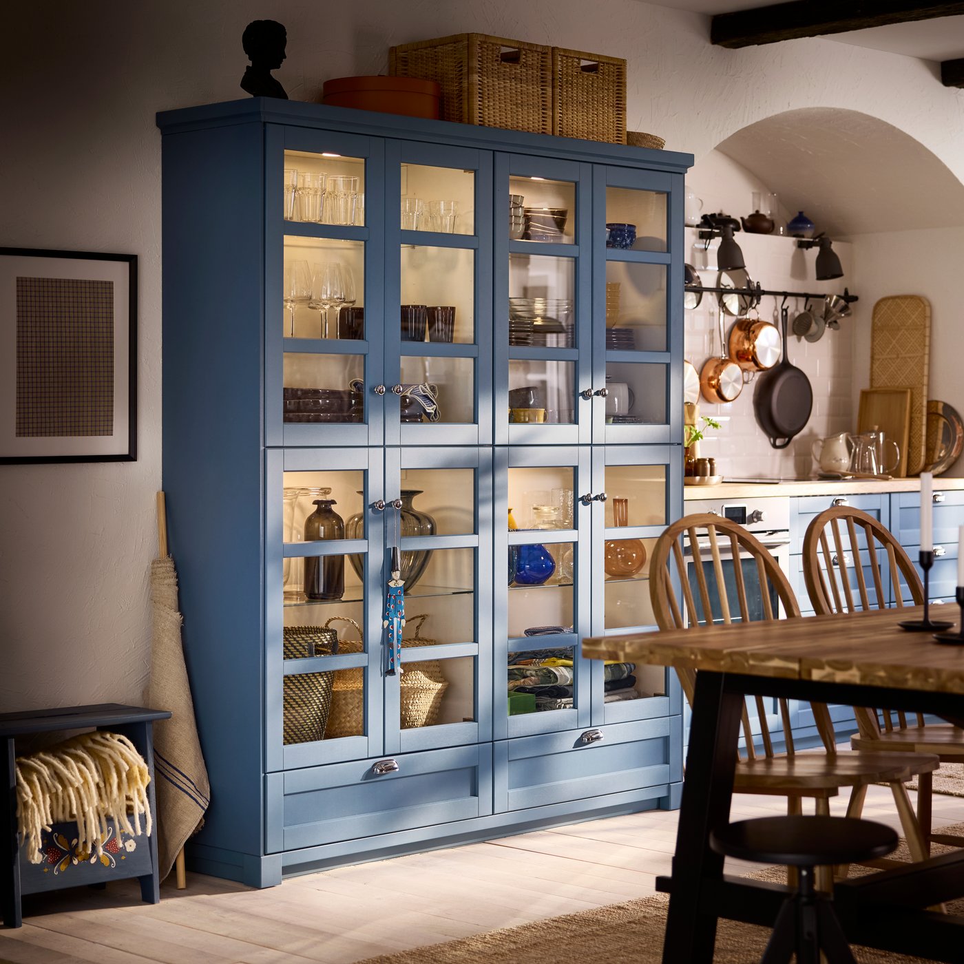 A dining table is standing in front of a piece of furniture made of METOD cabinets with glass doors in LERHYTTAN blue.
