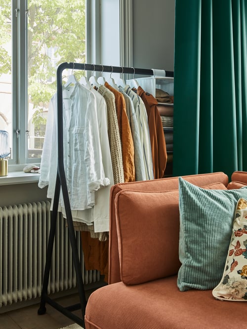 Salon avec portant noir pour l’intérieur et l’extérieur placé à côté d’un module de canapé-lit avec dossier.