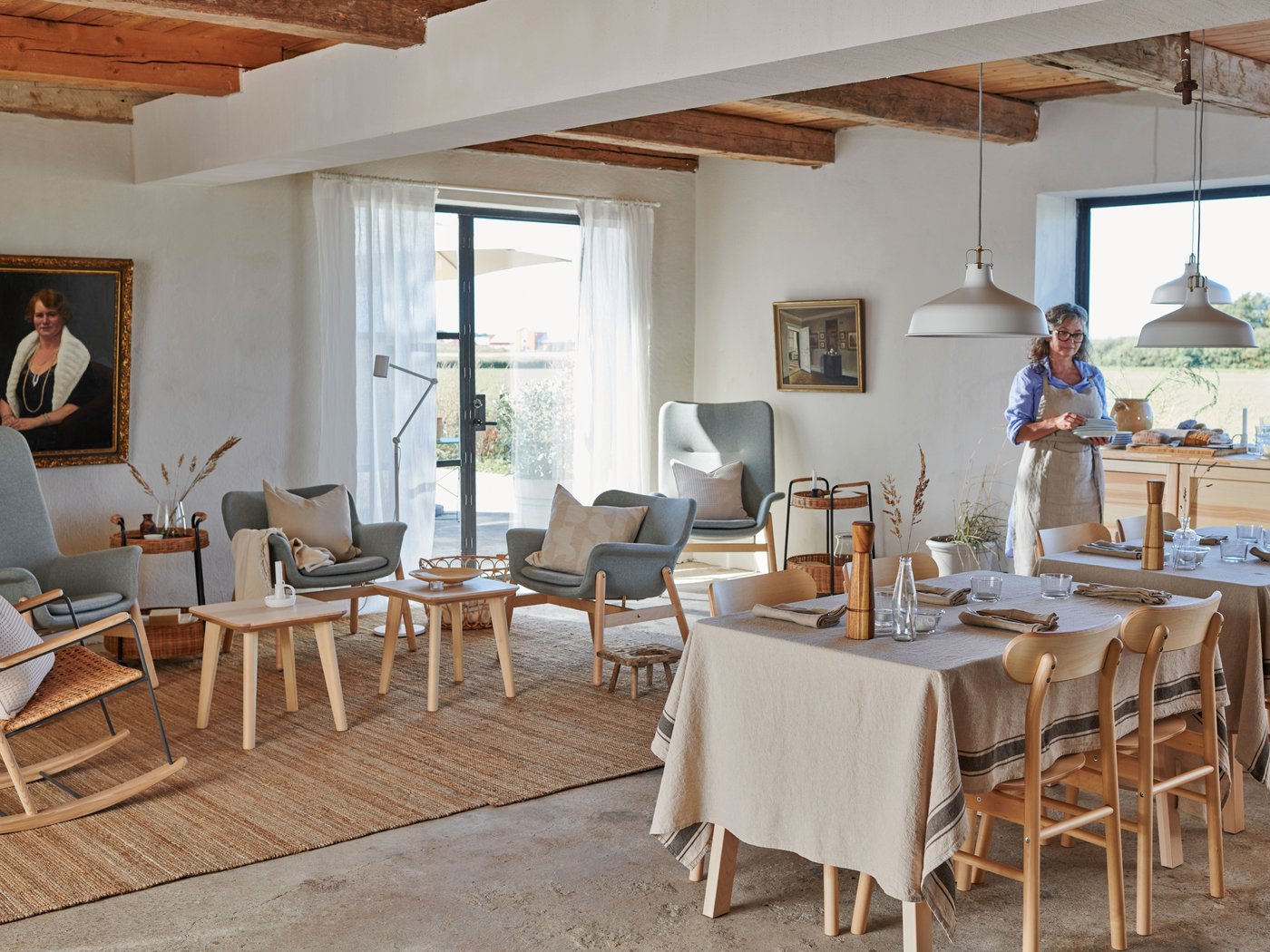 A large and bright living and dining space in traditional style with wooden beams in the ceiling and concrete floors.