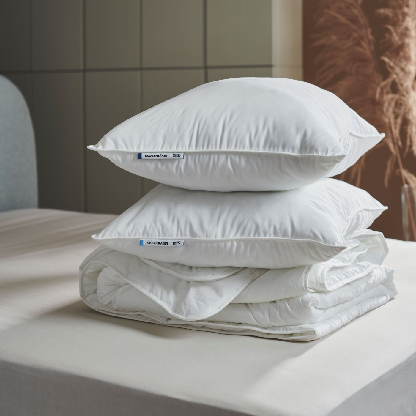 In einem modern eingerichteten Schlafzimmer liegen zwei hohe SKOGSFRÄKEN Kissen ohne Kissenbezug auf einer weißen Bettdecke.