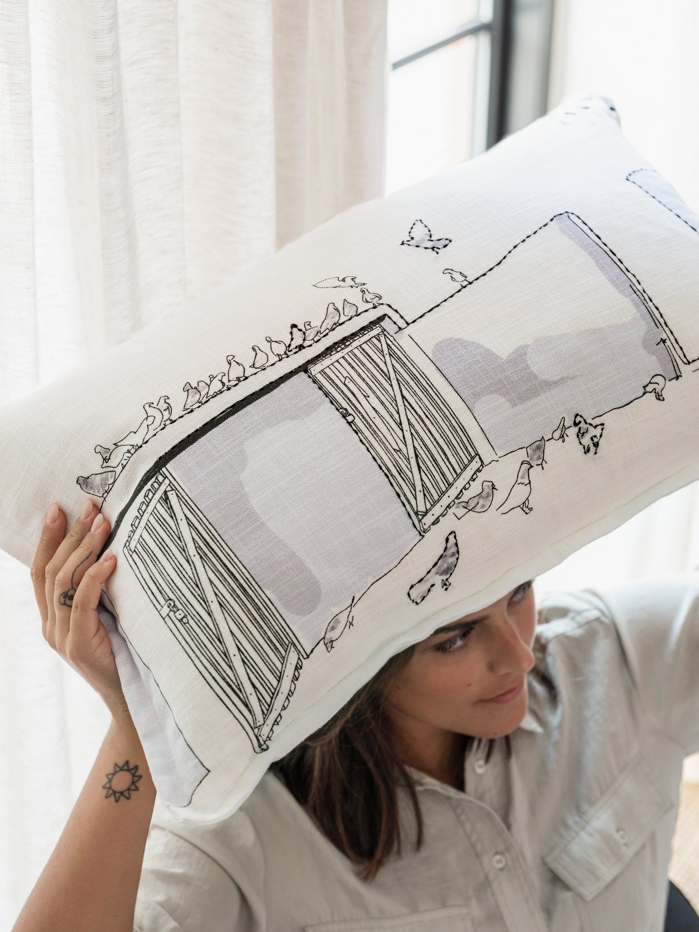 A woman holding up a hand-embroidered cushion showing a flock of pigeons on an Amman rooftop.