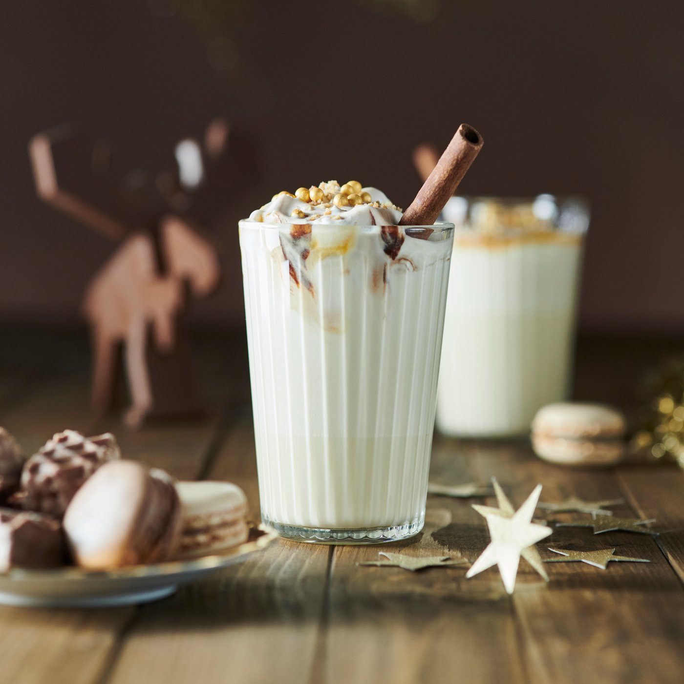 A tall glass with a white beverage, topped with whipped cream and a cinnamon stick, and a plate with assorted treats.
