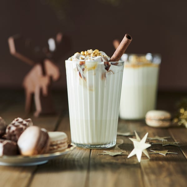 An IKEA VARDAGEN glass filled with a cream drink and a cinnamon stick. Various biscuits and chocolates around on smal plates.
