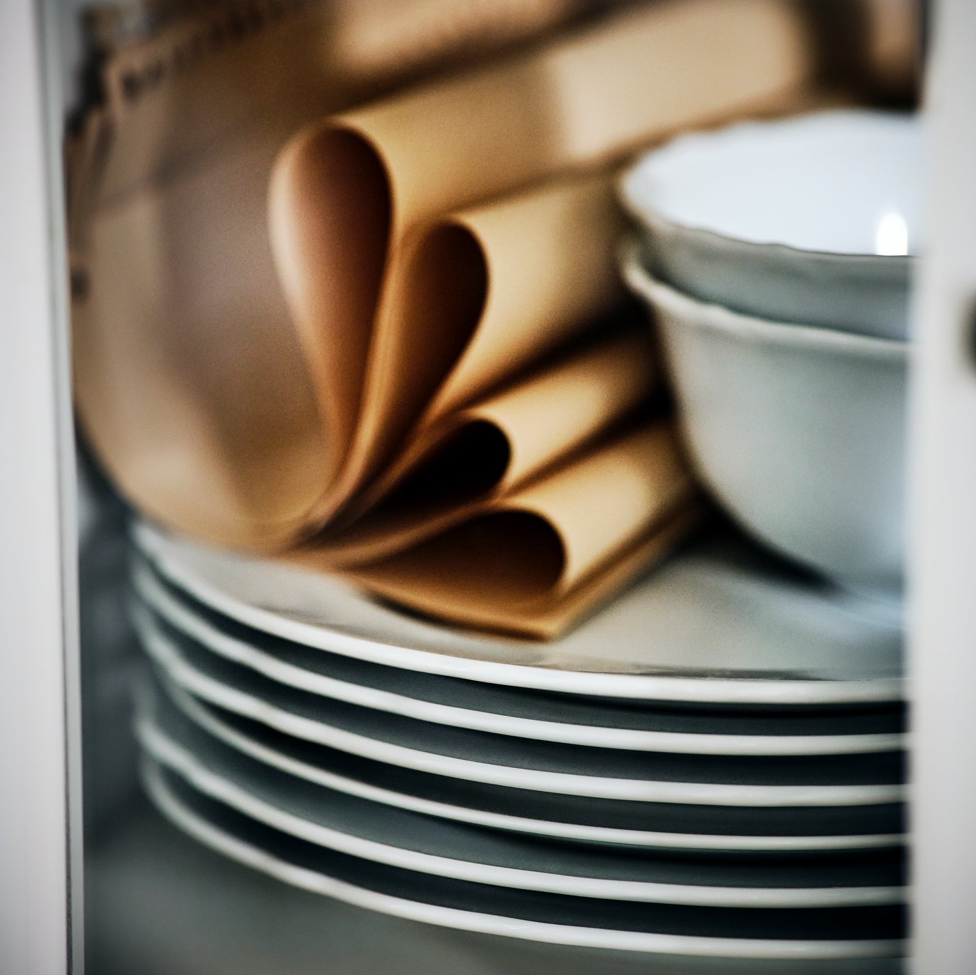 A pile of white UPPLAGA plates with two UPPLAGA bowls on top, along with several light brown napkins.
