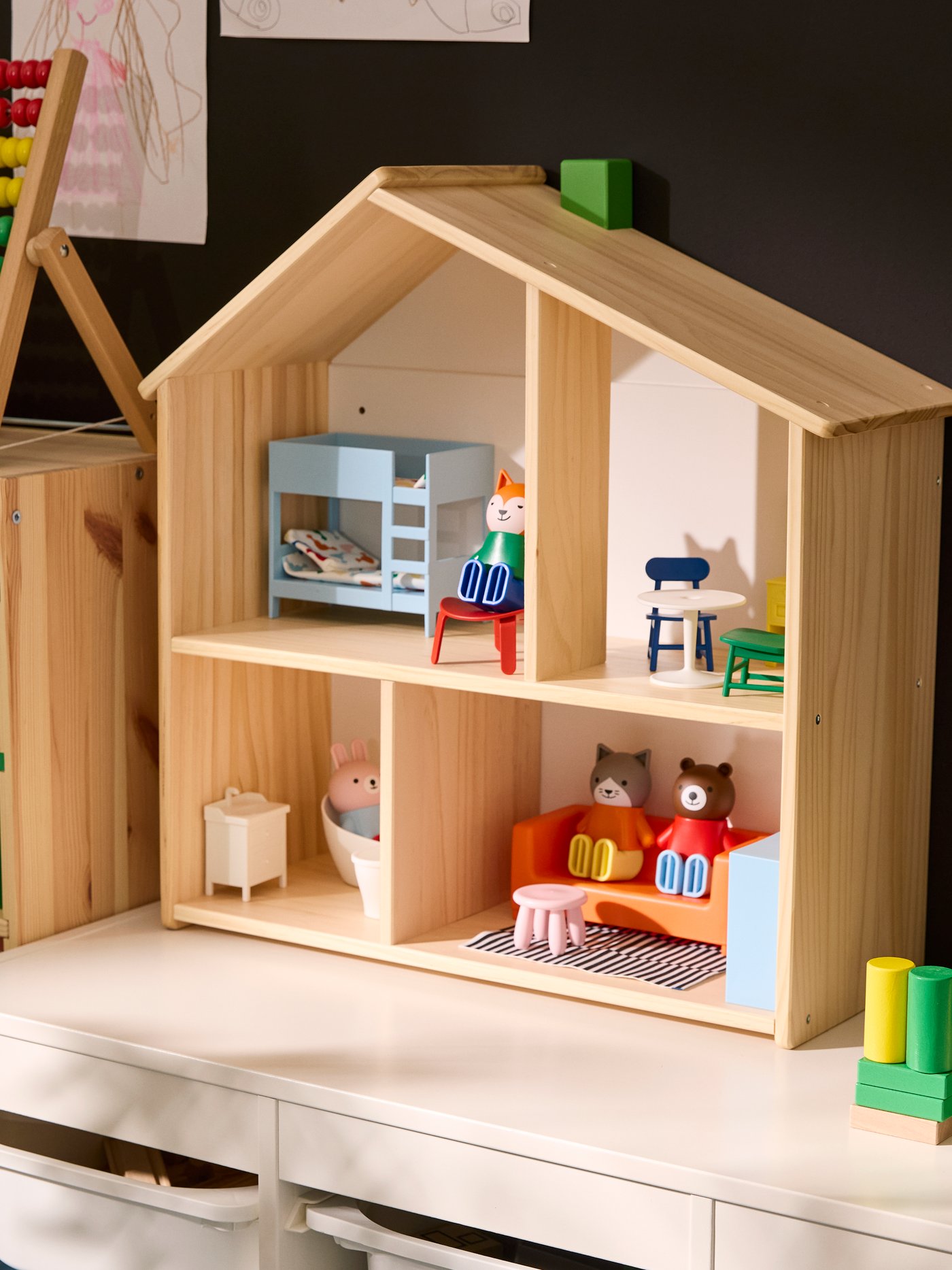 FLISAT doll’s house standing on TROFAST storage unit, with the house furnished with HUSET doll’s figures and furniture.