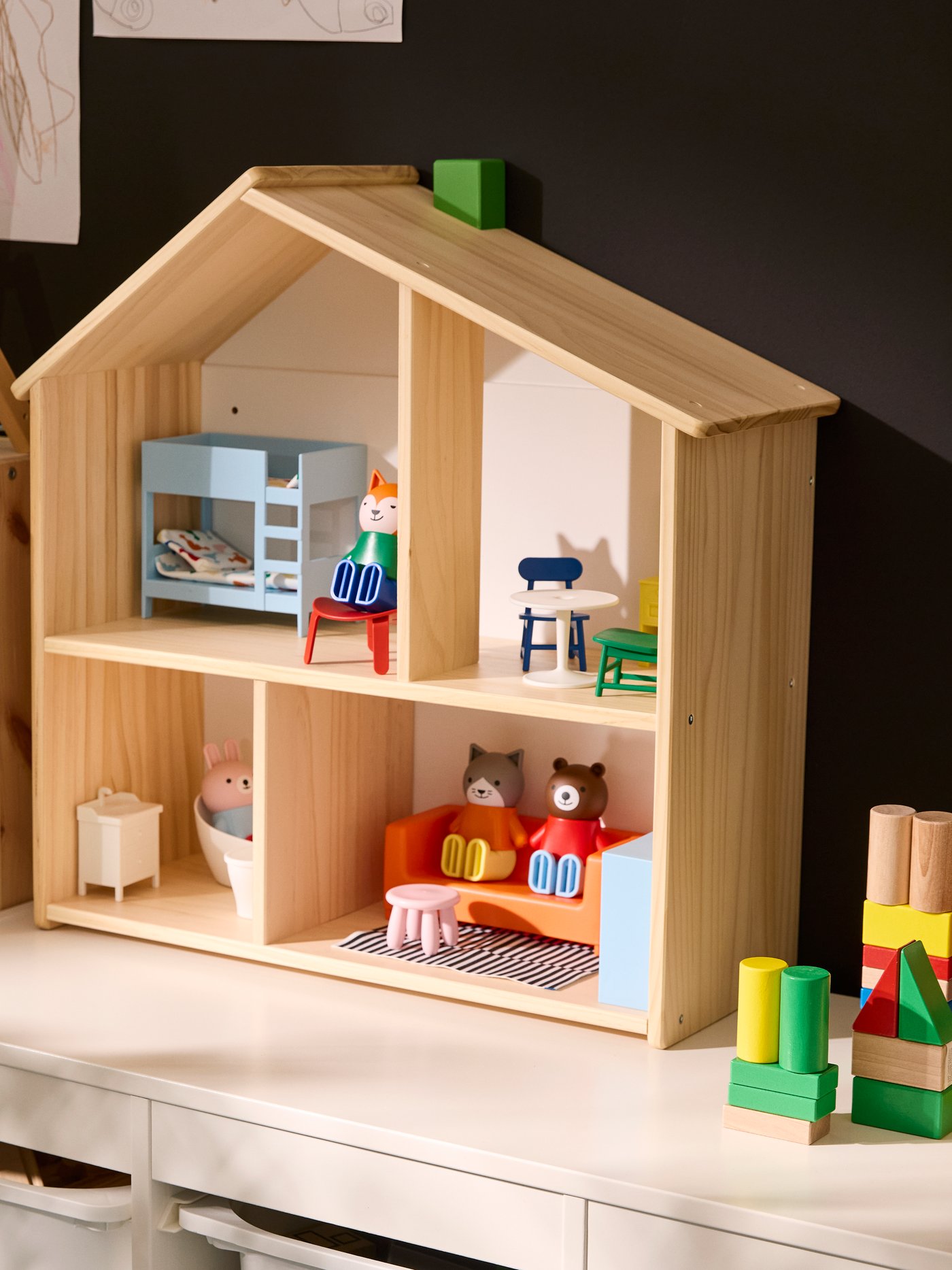 FLISAT doll’s house standing on TROFAST storage unit, with the house furnished with HUSET doll’s figures and furniture.