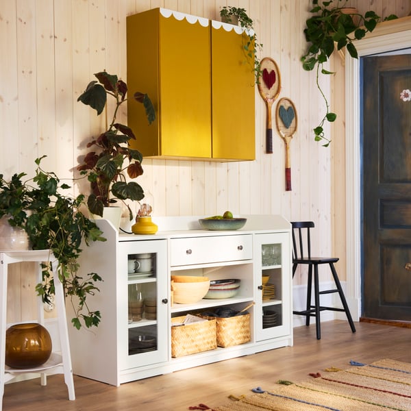 An IVAR cabinet, painted yellow and white, is mounted on the wall above a white HAUGA sideboard holding MJÖLKKANNA baskets.