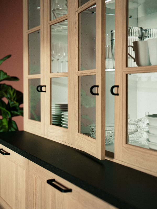 Kitchen cabinets consisting of VEDHAMN oak drawers and glass fronts are filled with white plates and glasses.