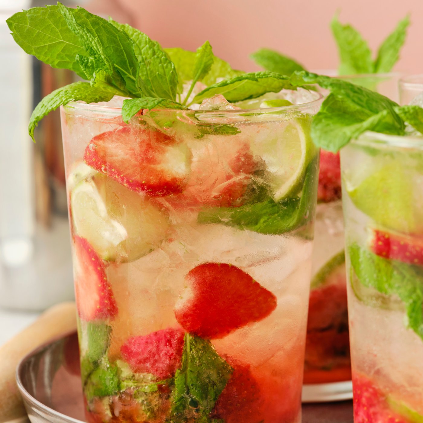 A glass filled with ISKUB lemon lime soft drink, strawberries and mint served on a silver tray.
