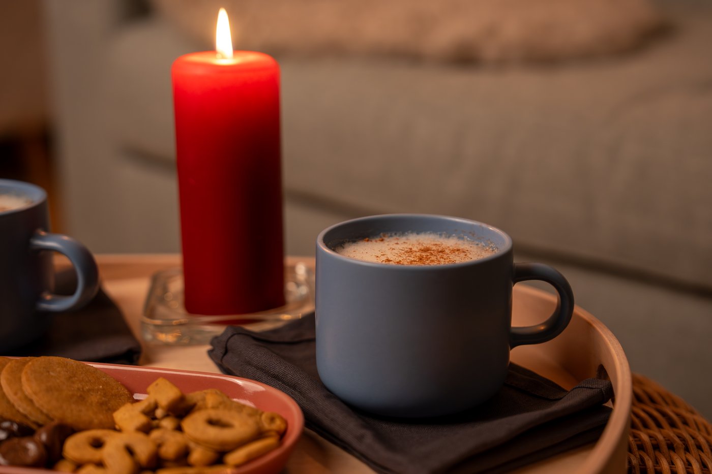 Zwei Tassen schwedischer Kakao mit einem Keksteller und einer roten Kerze auf einem Tisch präsentiert.