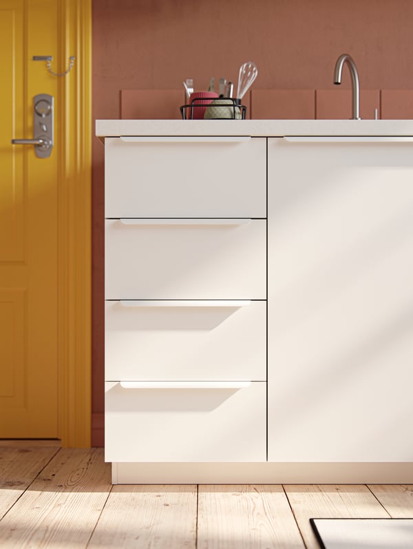 Mobili con frontali per cucina VALLSTENA bianchi, una parete e una fila di piastrelle color terracotta, una porta d'ingresso gialla.