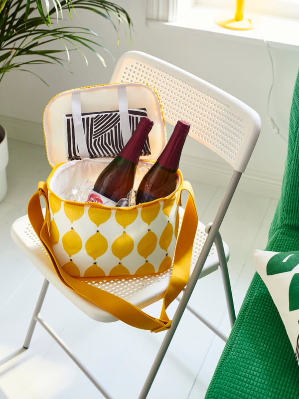 Bolsa para gardar alimentos en amarelo e branco con bebidas, colocada sobre unha cadeira pregable branca.