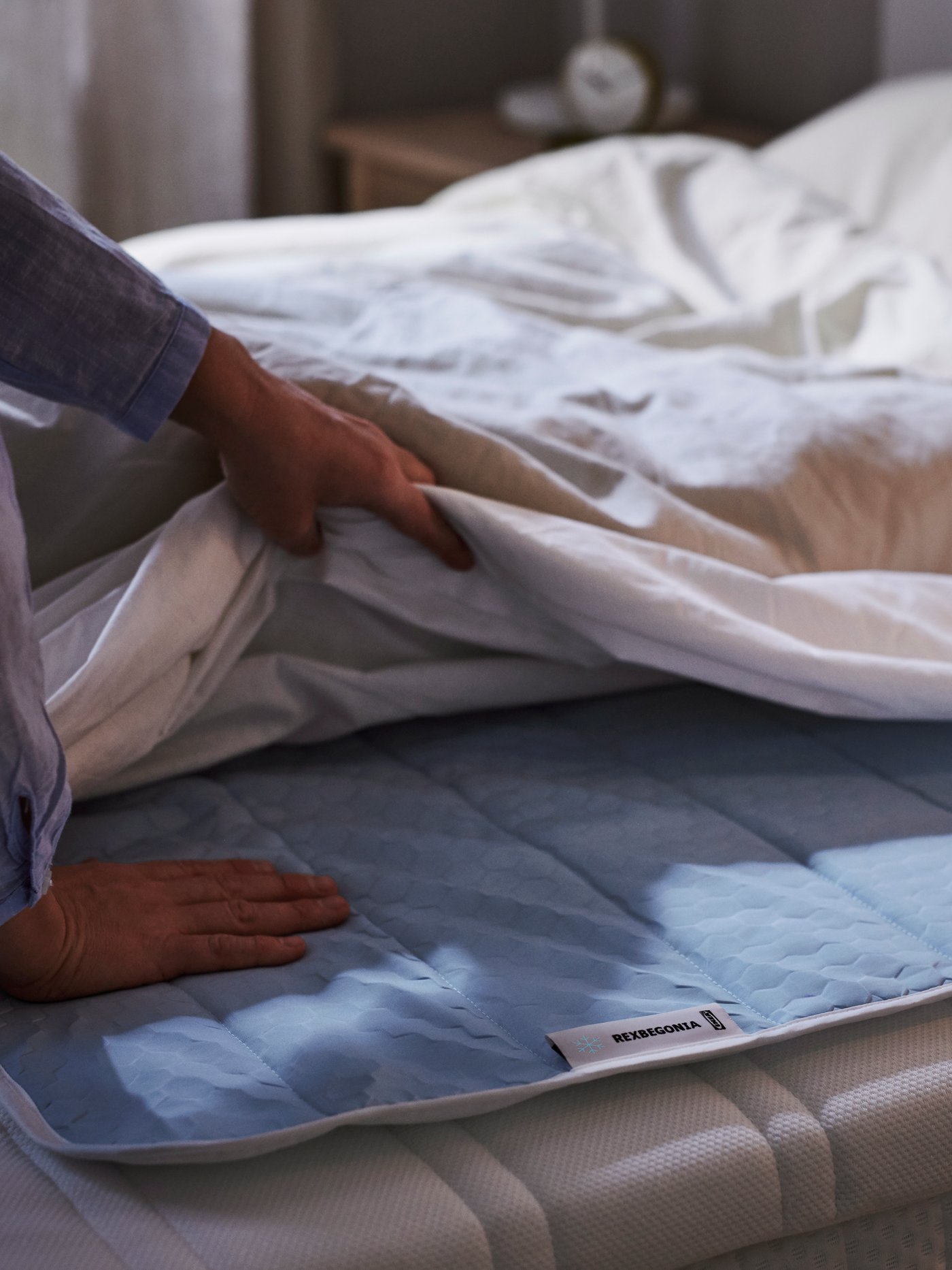 يد يمنى لشخص على لبادة REXBEGONIA الملطفة على سرير والأخرى تمسك ببعض البياضات.
