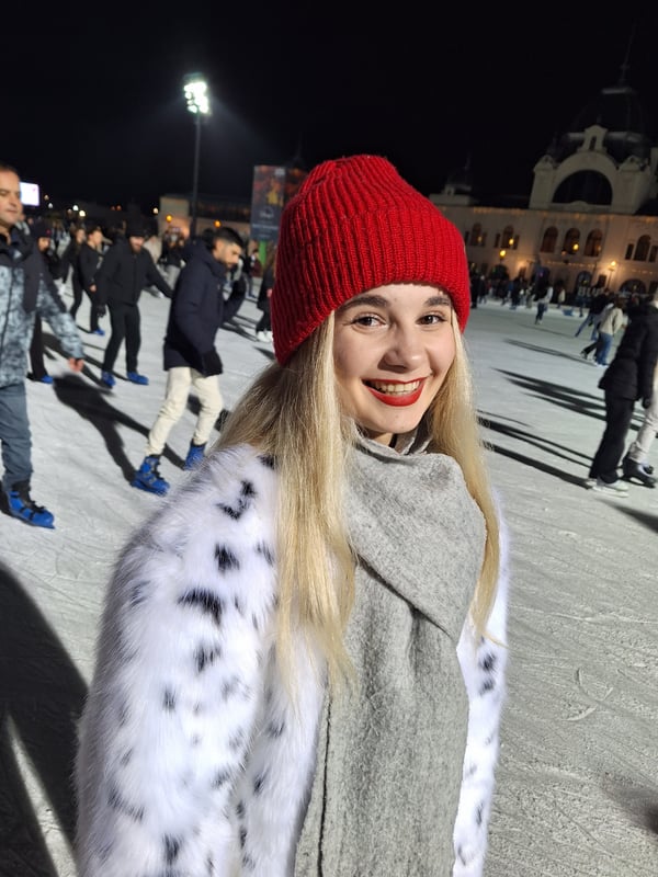 Yana in an ice rink wearing a red knitted cap, people are skating in the background.