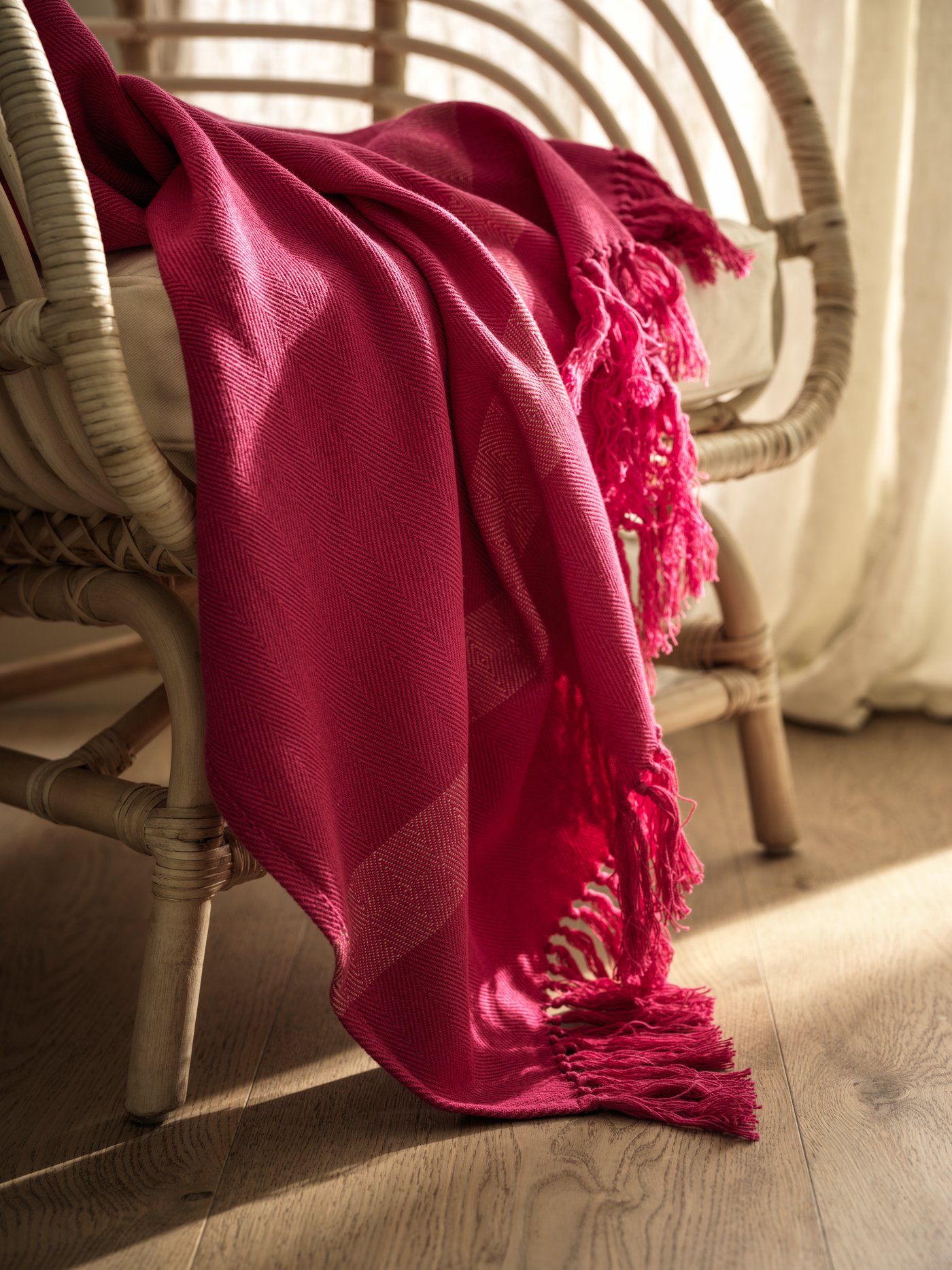Handmade HILLEGÄRD throw in pink on wooden chair on wooden floor in front of a white curtain.