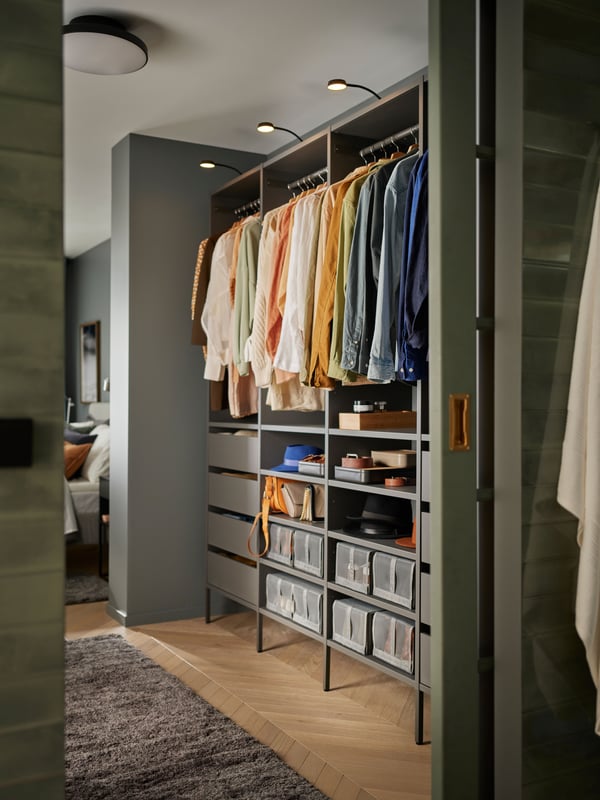 An open wardrobe combination in dark grey with both shelves, drawers, storage boxes and hanging clothes in perfect order.