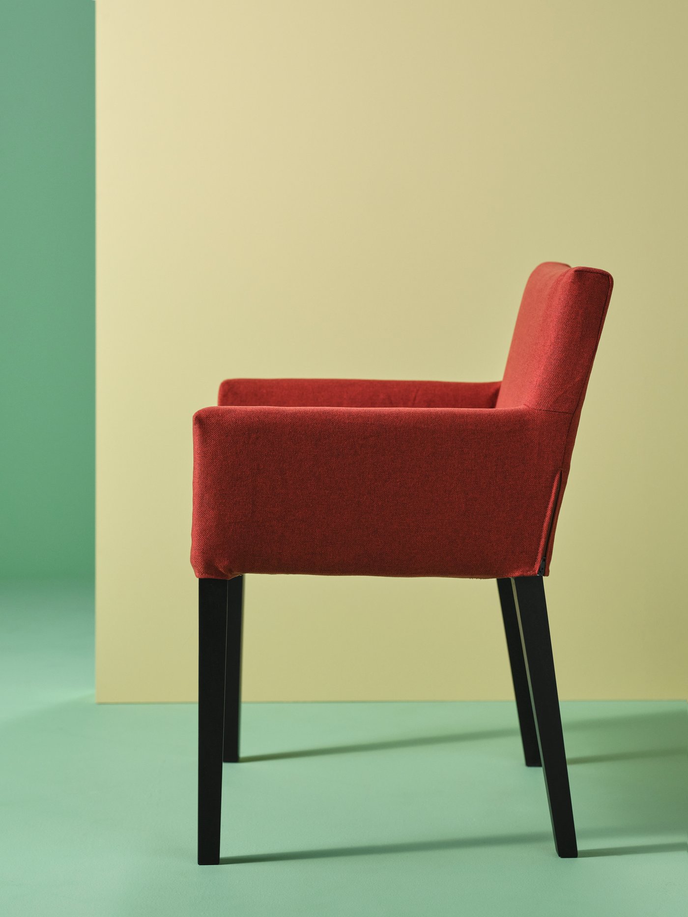 Salón con un primer plano de una silla MÅRENÄS roja con reposabrazos de madera maciza y una funda de poliéster.