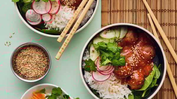 Two white bowls are placed on a light green table, and they are filled with a salad made of meatballs, rice and vegetables.