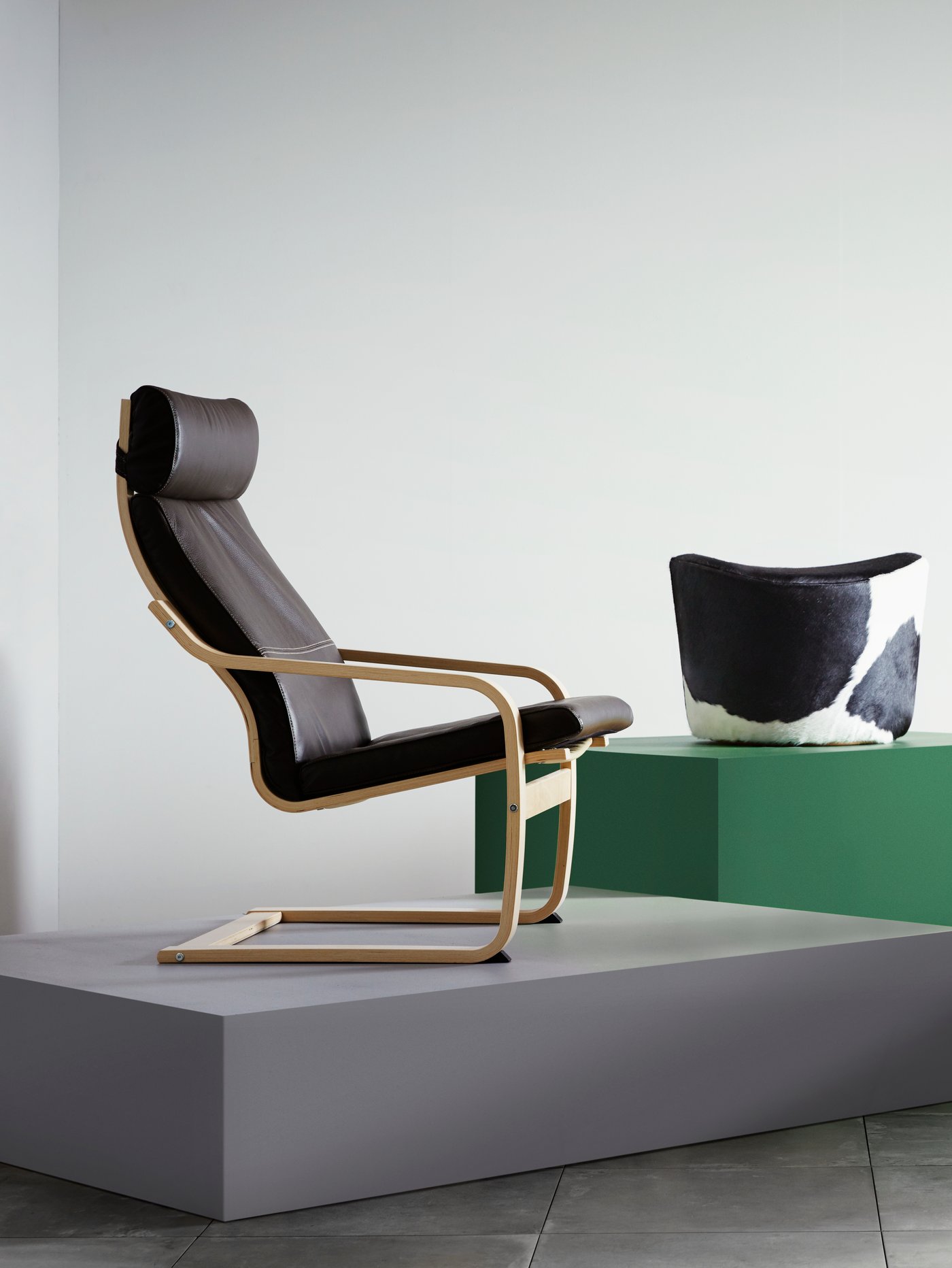 Salón con un sillón con respaldo alto sobre una plataforma gris y un puf sobre una plataforma verde.