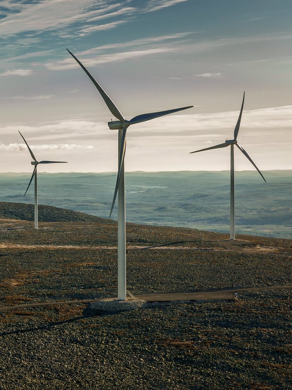 Several wind turbines stand tall on a hilly landscape, harnessing the power of the wind under a cloudy sky.