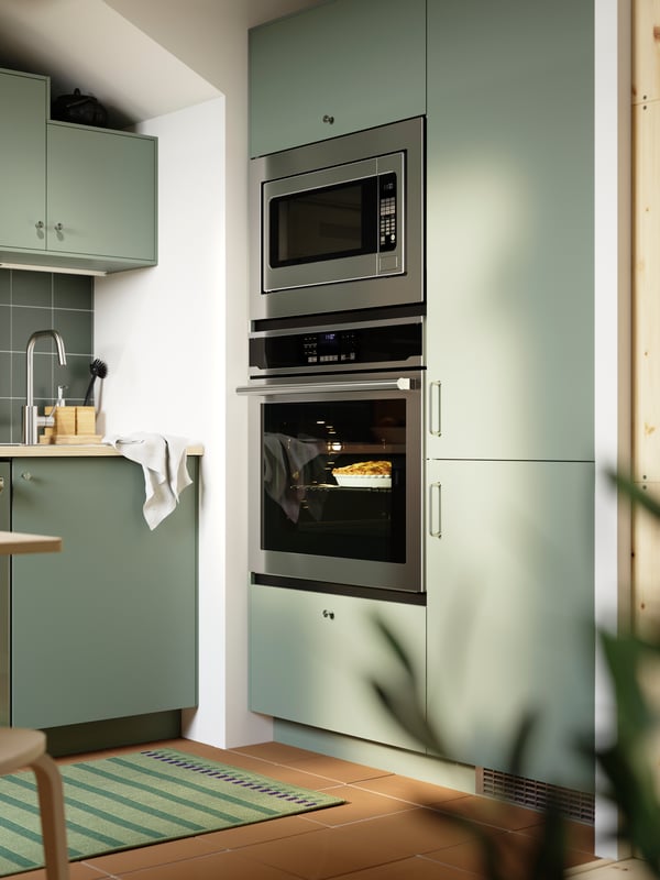 A kitchen with grey green NICKEBO fronts has a built-in oven, microwave oven, and a fridge/freezer with the same style front.