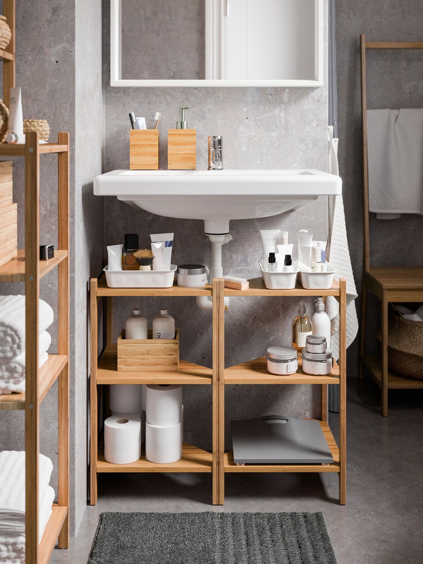 Two RÅGRUND corner shelves, made of bamboo, are placed below a white washbasin with bathroom products stacked on them.