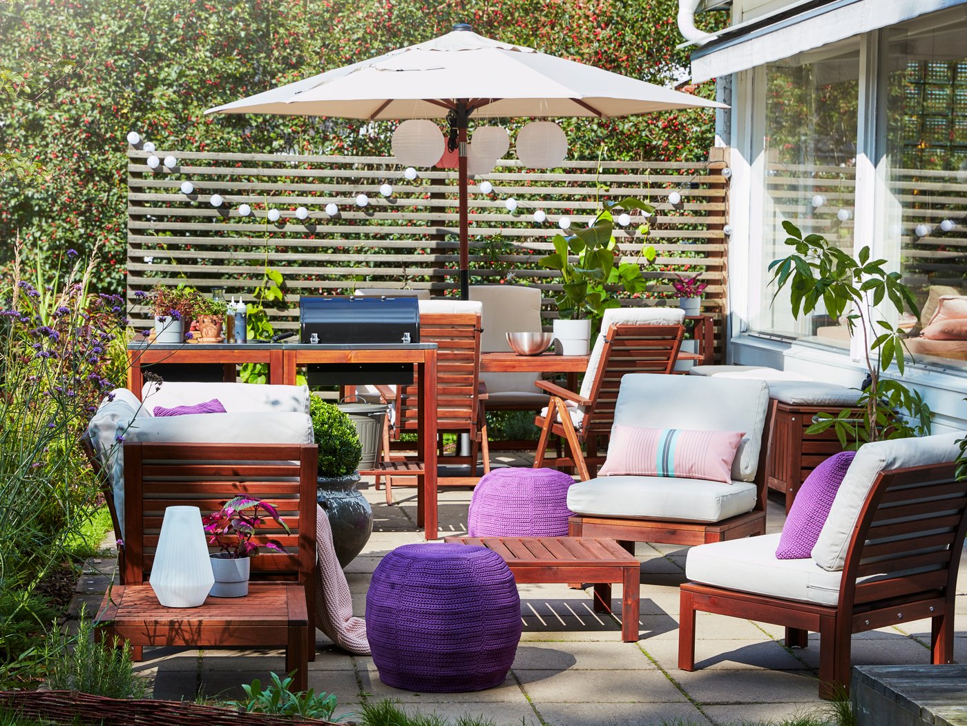 Spazio esterno con barbecue, set di mobili a 4 posti in acacia, ombrellone beige, pouf viola e cuscini da esterno beige.